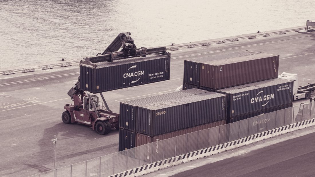 Reach stacker moving a shipping container at the port — our lots ship in 20' and 40' containers