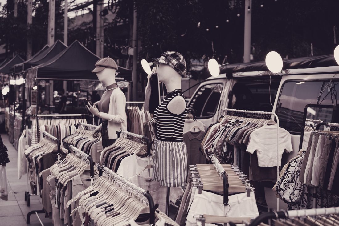 Evening street market with tops and trousers on rails, shoppers in front