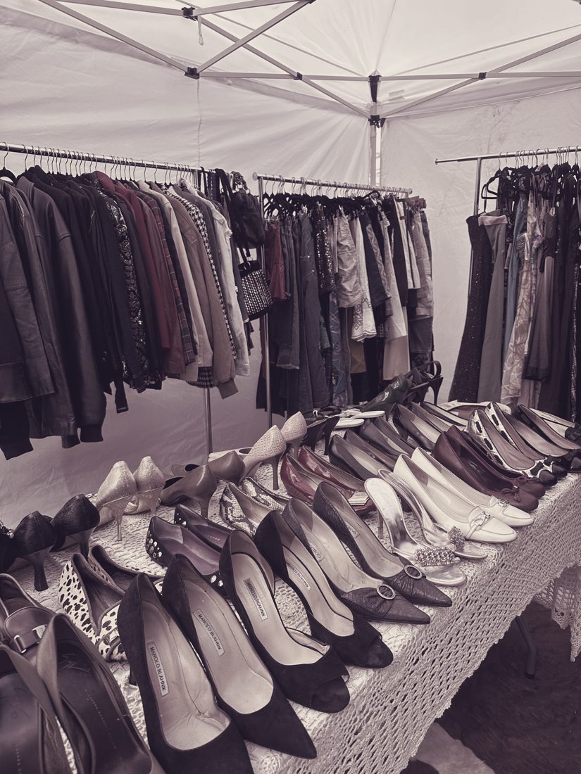 Shoe counter with heels and boots, clothing rails behind — footwear is sorted separately from apparel